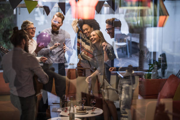 Large group of happy entrepreneurs dancing during office party. Group of happy creative people having fun while dancing during a party at casual office. The view is through glass. office parties stock pictures, royalty-free photos & images