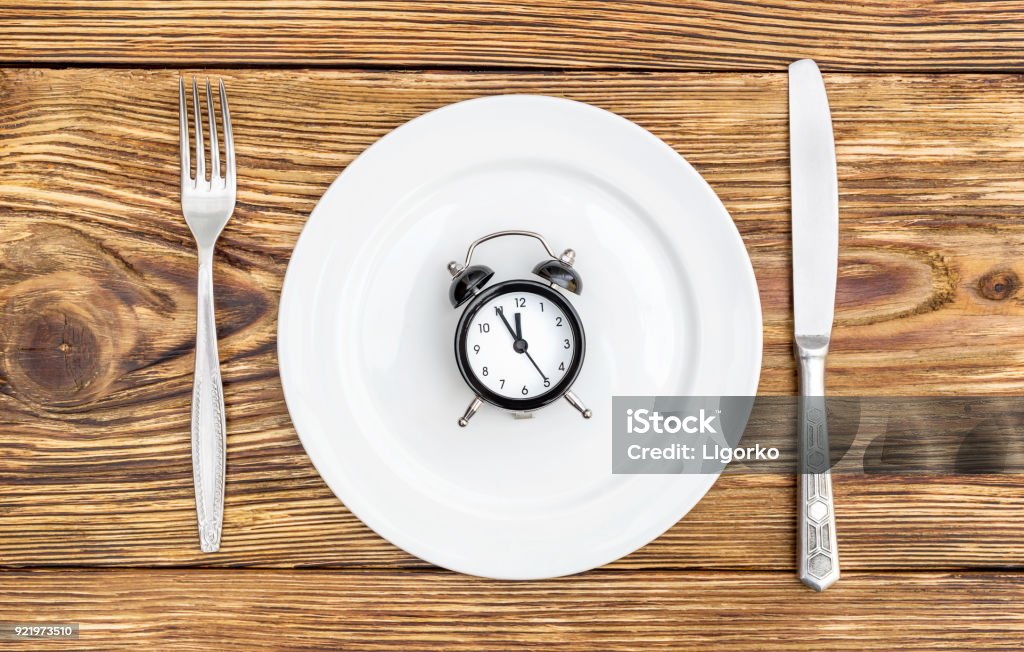 Alarm clock with fork, knife and plate on the table. Top view. Time to eat. Alarm Stock Photo