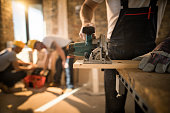 Unrecognizable worker cutting plank with circular saw at construction site.