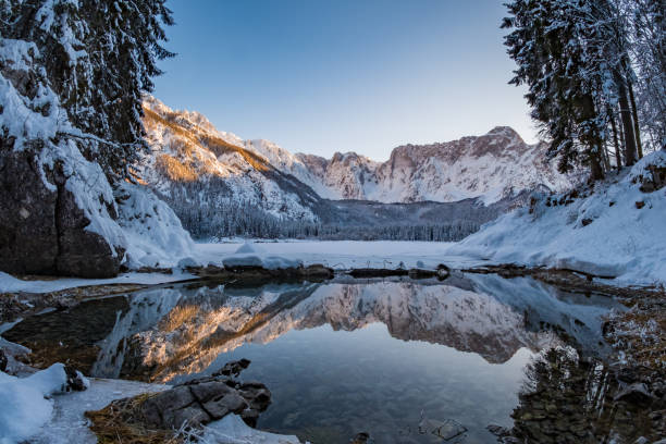 Mountain range Mangart reflecting in thawed part of lake Fusine Mountain range Mangart reflecting in thawed part of lake Fusine in Italy julian california stock pictures, royalty-free photos & images