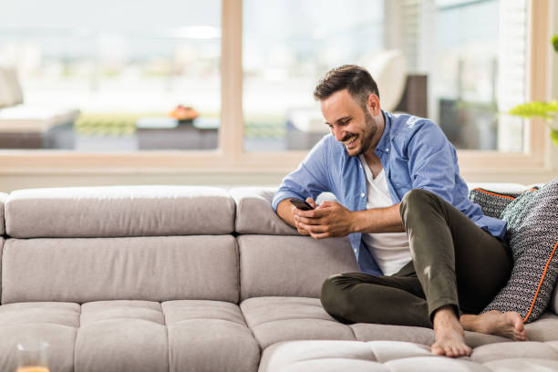 istock Happy man text messaging on mobile phone while relaxing in living room. 921987854