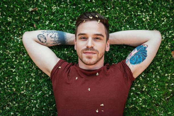 istock Cheerful young man with tattoos relaxing in park on green grass 921990868