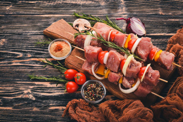 istock Raw kebab from meat on a wooden background with vegetables. Top view. Free space for text. 922000732