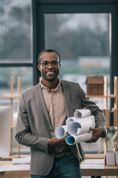 cheerful african american architect holding blueprints in office