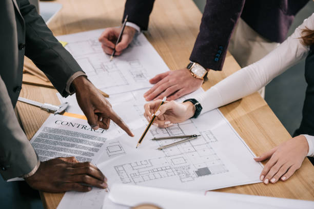 istock cropped view of multiethnic architects discussing and working with blueprints and documents in office 922006460