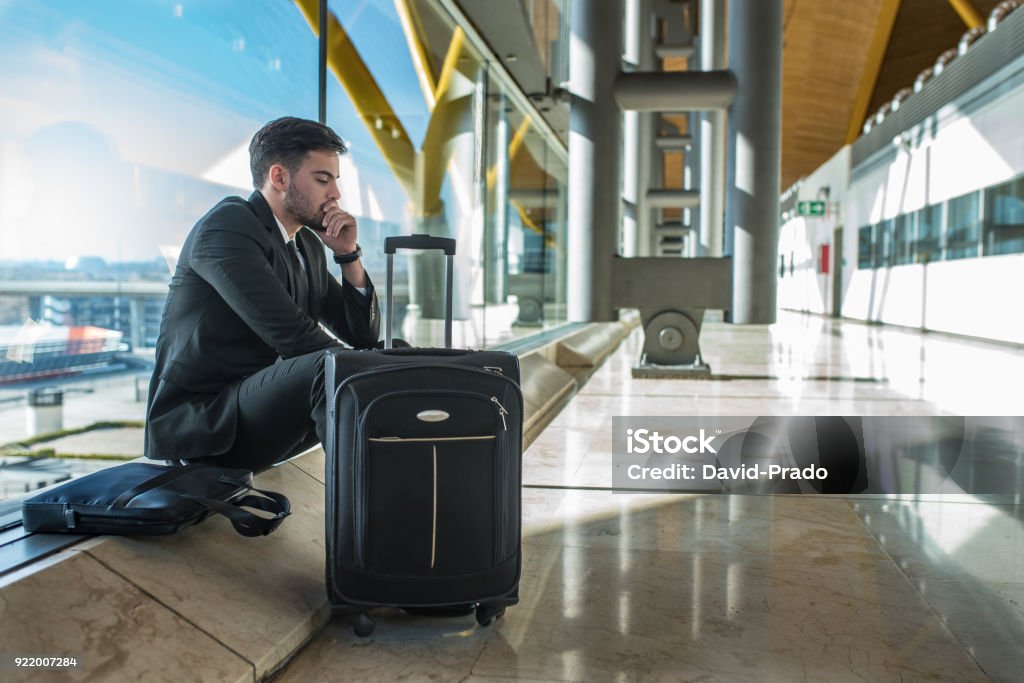 young businessman upset at the airport waiting his delayed flight with luggage Airport Stock Photo