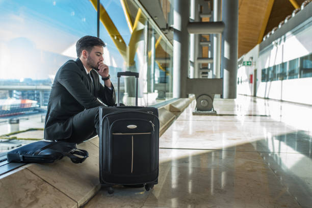 young businessman upset at the airport waiting his delayed flight with luggage stock photo