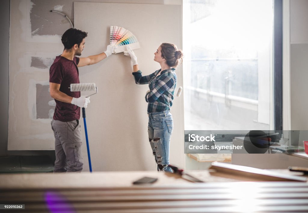 Young couple choosing the right color for their wall while renovating apartment. Young couple choosing the right color for their wall in new apartment. Painting - Activity Stock Photo