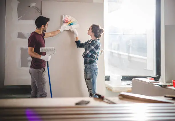 Photo of Young couple choosing the right color for their wall while renovating apartment.