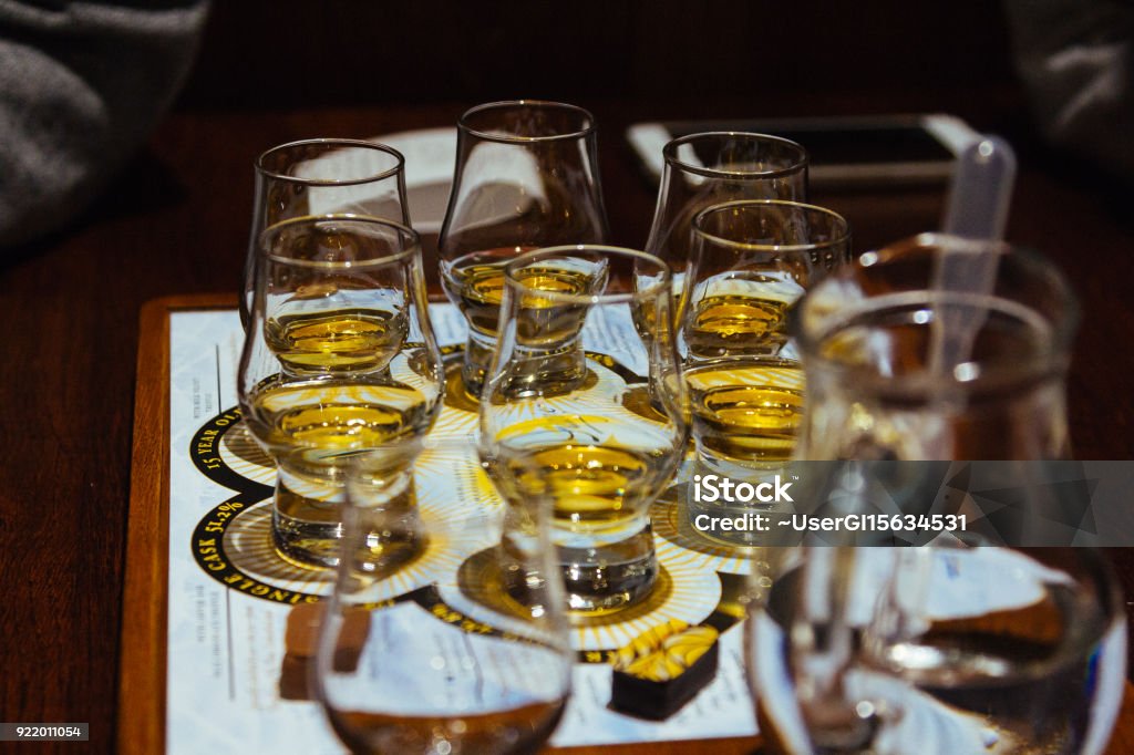 A whisky tasting flight of six glasses on a table A set of six small glasses is set out ready for a whisky tasting flight. The glasses are on a sheet of paper and there is a jug of water in the foreground. Whiskey Stock Photo