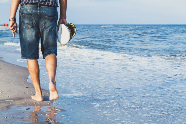 homme marchant sur la plage de la mer - shorts rear view summer beach photos et images de collection