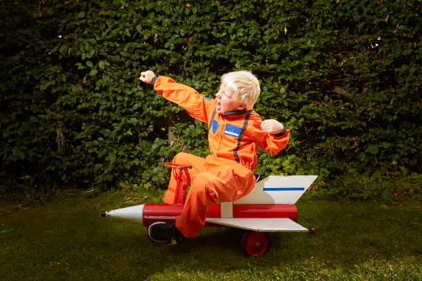 Children sit / play on a soapbox rocket outdoors in the garden