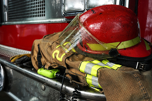 Portrait of a firefighter using holding a fire hose while his colleague is storing a chainsaw inside of a fire truck equipment compartment