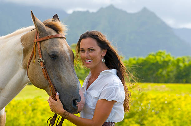An attractive woman laughing outside while standing outside with her horse
