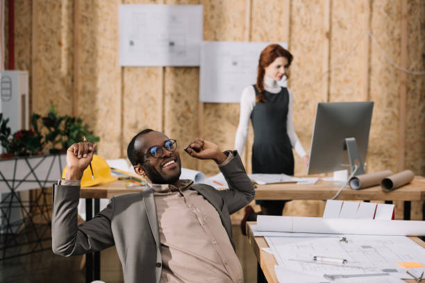 istock handscome african american architect stretching in chair while his colleague working with computer 922044588
