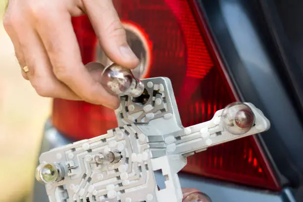 The mechanic's hand inserts the bulb into the frame rear lamp of the car.