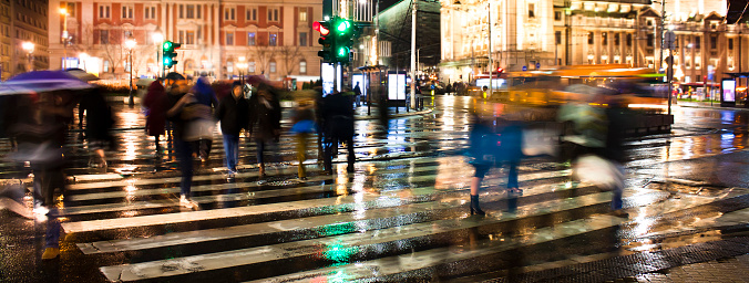 Blurry people silhouettes crossing the city street in motion blur in rainy night