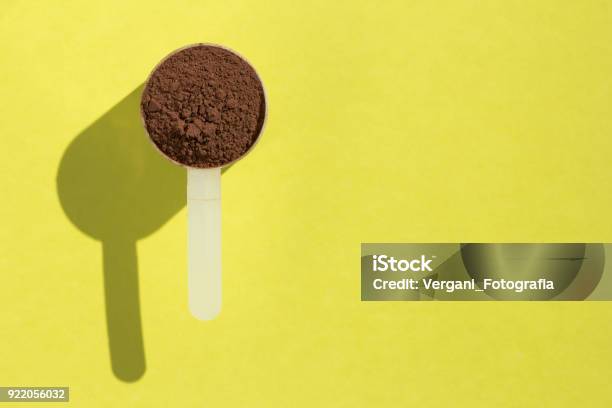 Whey Protein Minimalism And Hard Light Measuring Scoop Full With Chocolate Flavour Powder On Yellow Background Stock Photo - Download Image Now