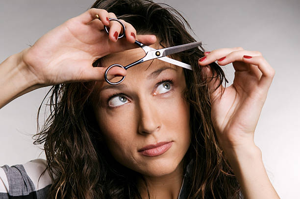 Young woman using scissors to cut her bangs  young woman cutting her fringe over grey background bangs hair stock pictures, royalty-free photos & images