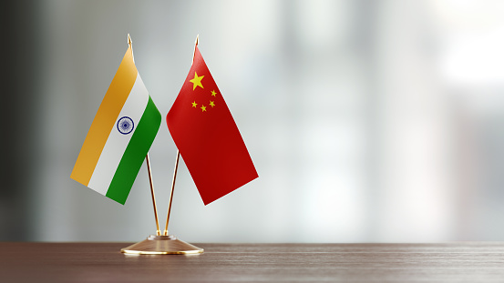 Indian and Chinese flag pair on desk over defocused background. Horizontal composition with copy space and selective focus.