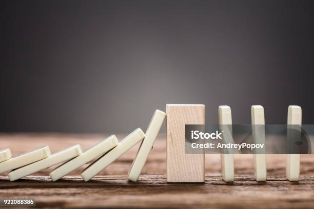 Wooden Block Amidst Falling And Upright Domino Pieces On Table Stock Photo - Download Image Now