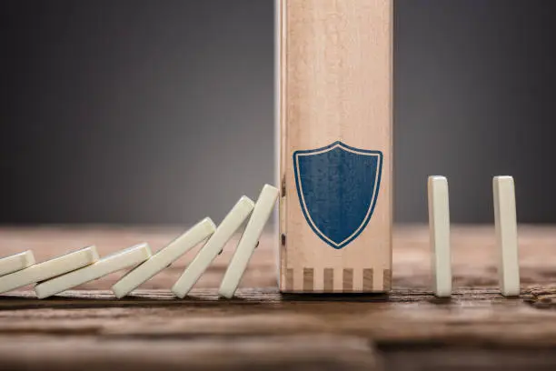 Closeup of wooden block with shield symbol amidst falling and upright domino pieces