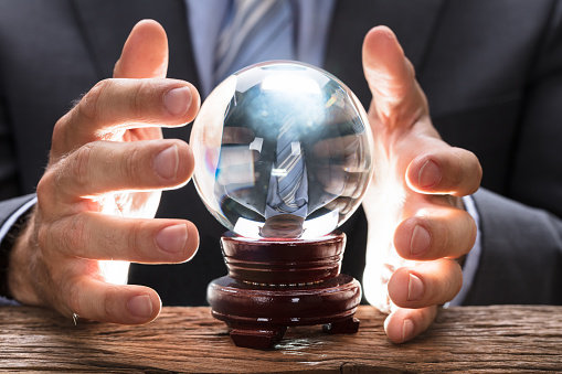 Midsection of businessman covering crystal ball at wooden table
