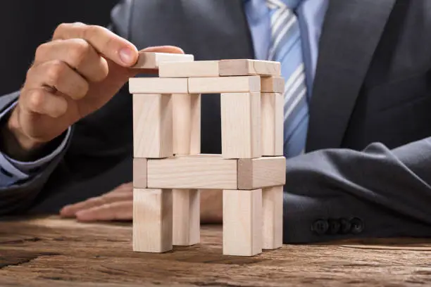 Midsection of businessman building tower with wooden blocks at table