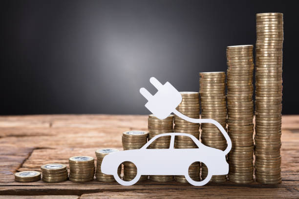 istock Electric Car Against Stacked Coins On Wooden Table 922106790
