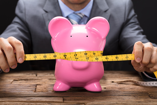 Midsection of businessman squeezing piggybank with tape measure on wooden table