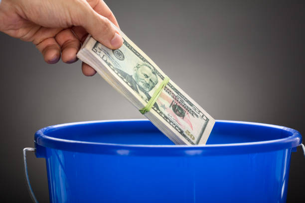 istock Hand Throwing Us Paper Currency Bundle In Blue Bucket 922107184