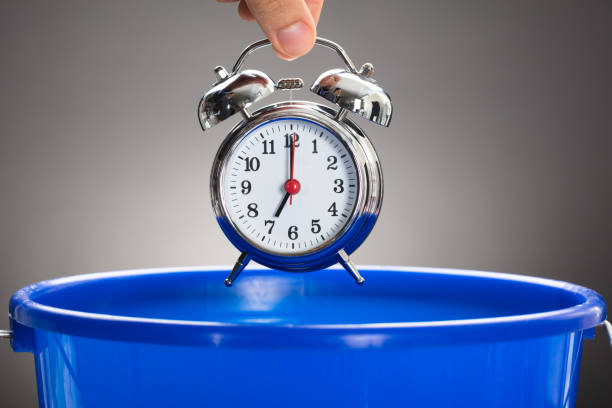 businessman's hand throwing alarm clock in blue bucket - misapplication imagens e fotografias de stock