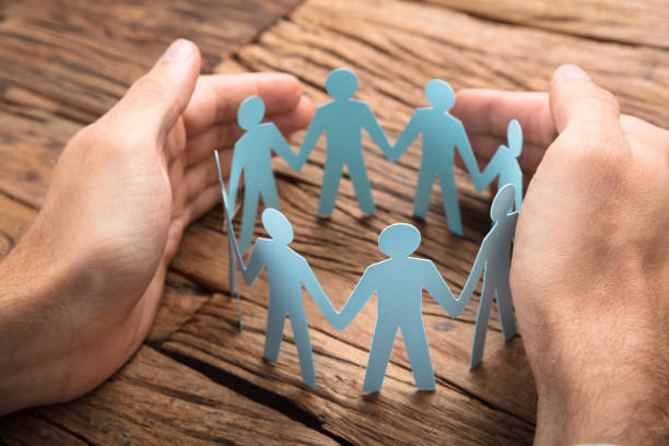 Businessman's Hands Covering Paper Team On Table Cropped image of businessman's hands covering paper team on wooden table supported stock pictures, royalty-free photos & images