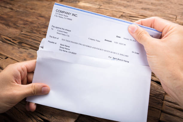 Businessman's Hands Holding Cheque At Table Cropped hands of businessman holding cheque at wooden table paycheck photos stock pictures, royalty-free photos & images