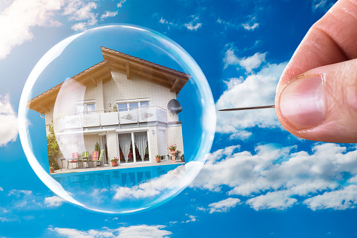 Human Hand Poking House And Bubble With Needle Against Cloudy Sky