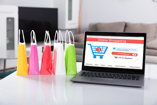 Multi Colored Shopping Bag Besides Laptop With Online Shopping Website On Screen