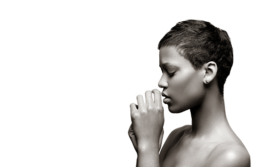 Side view of a young African woman praying against gray background with copy space to the left.