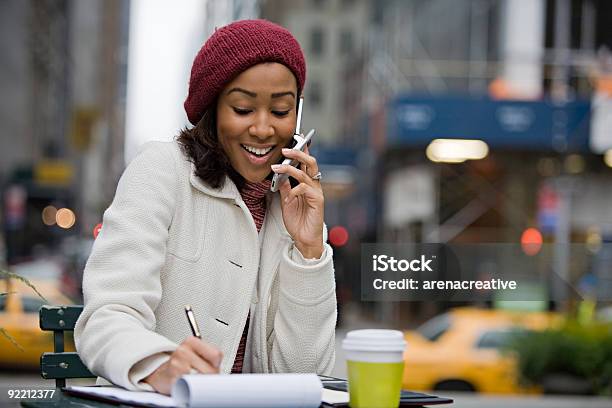 Woman At An Outdoor Cafe Chatting On Her Phone And Writing Stock Photo - Download Image Now