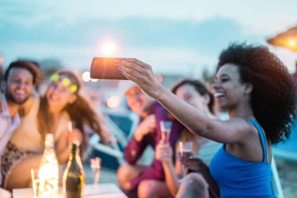 幸せのお友達が楽しんで飲むバーのシャンパン キオスク - モバイル携帯電話にソフト フォーカス - 若者のライフ スタイルと休暇コンセプトで若い人たちのビーチ パーティー - 屋外でスマー - friendship party young adult beach ストックフォトと画像