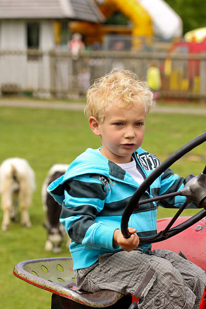 A tween boy climbs into the tractor beside his father to learn how to operate the equipment during hay harvest season on their family ranch in Wyoming.