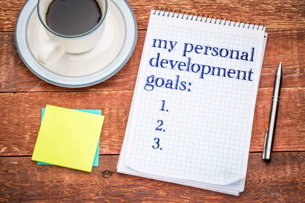 My personal development goals list Handwriting in a spiral notebook, sticky notes and a cup of coffee against rustic wood