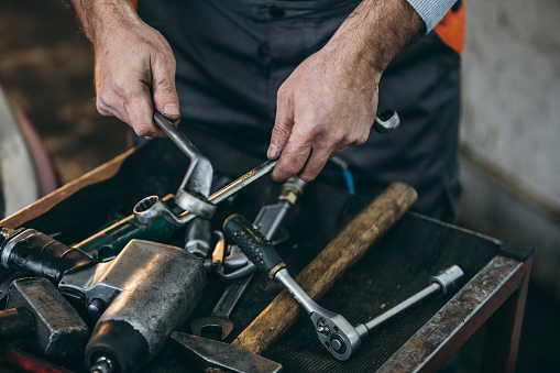 One man, mature adult auto mechanic holding work tools in auto repair shop, part of.