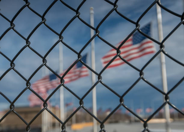 American Flags at Half Mast behind Chain Link Fencing stock photo