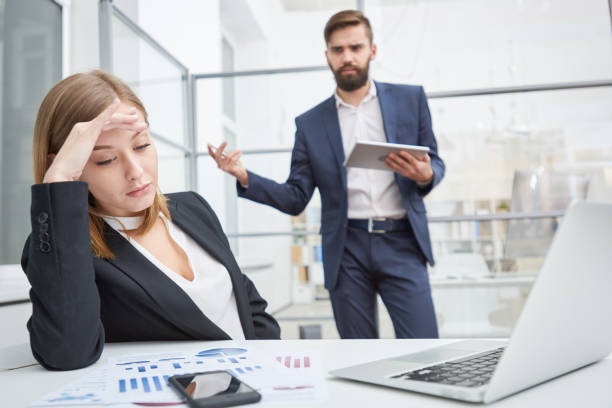 Displeased boss berating indifferent employee Angry displeased employer unsatisfied with employees work and berating young female manager leaning on hand and looking at report indifferently bossy stock pictures, royalty-free photos & images