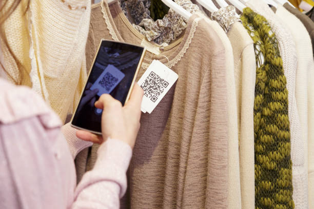 Woman scanning a QR code from a label. Woman scanning a QR code, with her smart phone, from a label in a clothing store. No face. scanning activity stock pictures, royalty-free photos & images