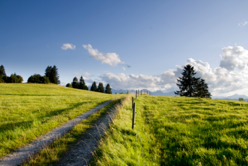 A gravel road winds through lush mountains under a blue sky