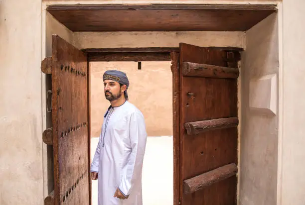 omani man in traditional outfit walking through old wooden door