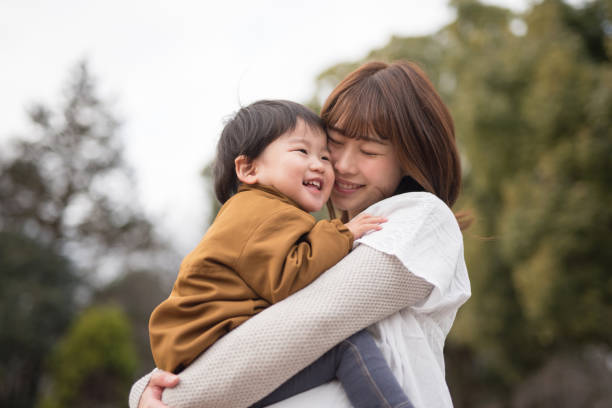 母親の腕の中で子を保持 - 日本人　親子 ストックフォトと画像