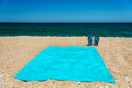 Blue sandal flip flop and towel on yellow sand. Summer fun time and accessories on the beach, summer vacations, copy space.