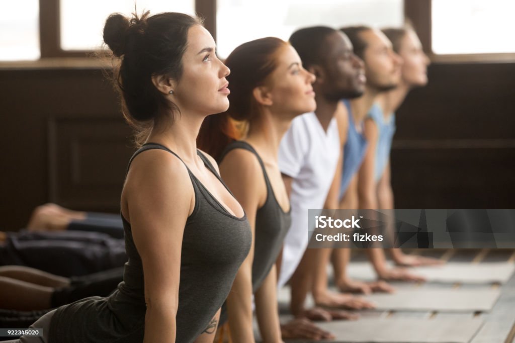 Group of sporty people in upward facing dog exercise Group of young sporty afro american and caucasian people practicing yoga lesson, stretching in upward facing dog exercise, Urdhva mukha shvanasana pose, working out, indoor close up, studio side view Yoga Stock Photo